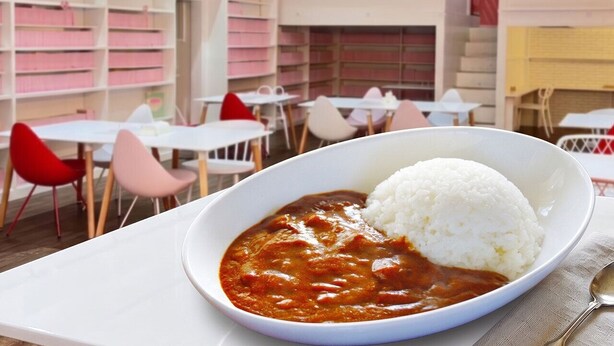 Un tazón de curry con arroz sobre un plato blanco, un mantel blanco y sillas rojas en un café.