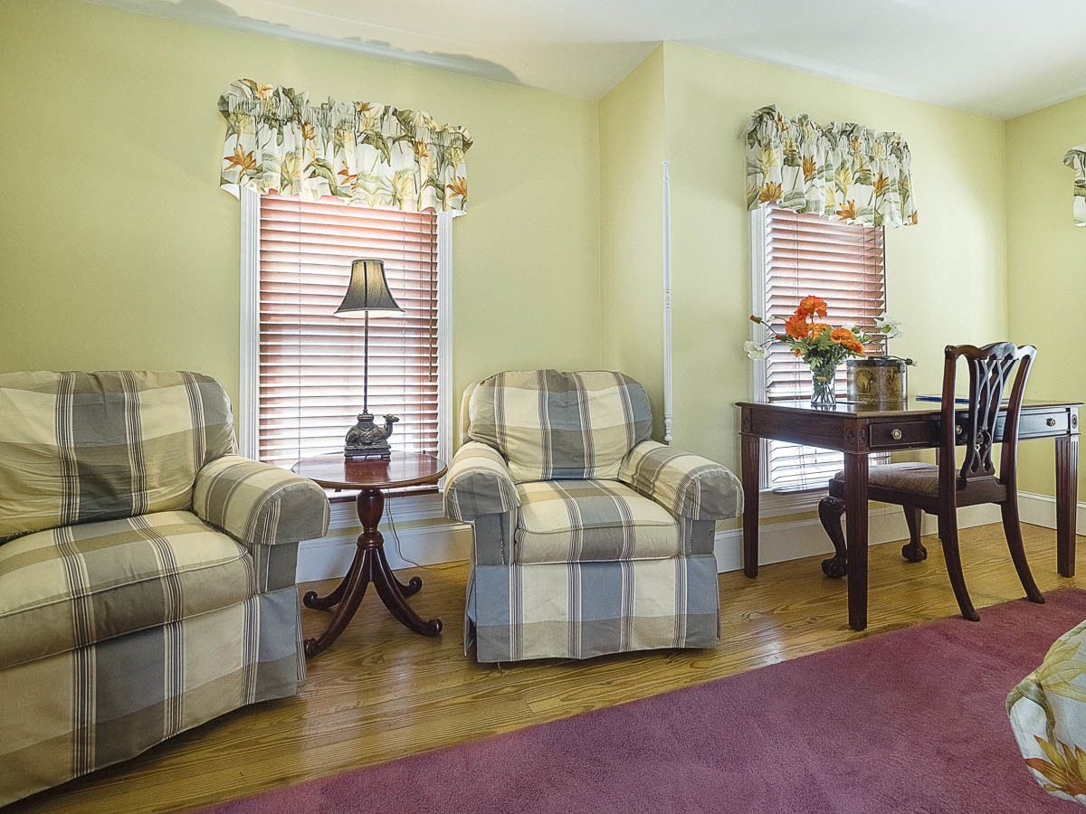 A living room with two plaid sofas, a wooden coffee table, a dining table with chairs, and a vase with flowers.