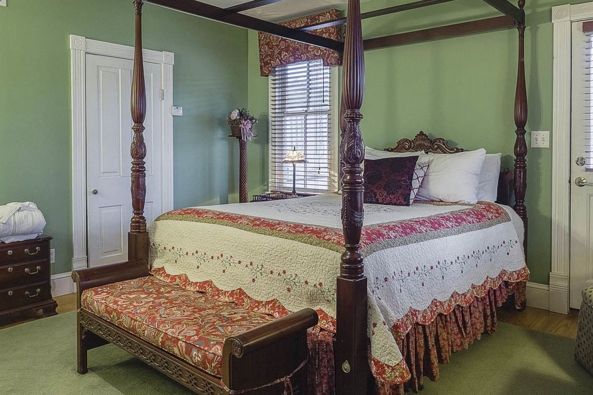 A four-poster bed with a floral bedspread, a nightstand with a lamp, and a dresser with drawers.