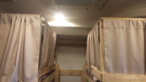Ein schmaler Korridor mit Etagenbetten an beiden Seiten, einem Deckenlüfter und einer Leuchte.