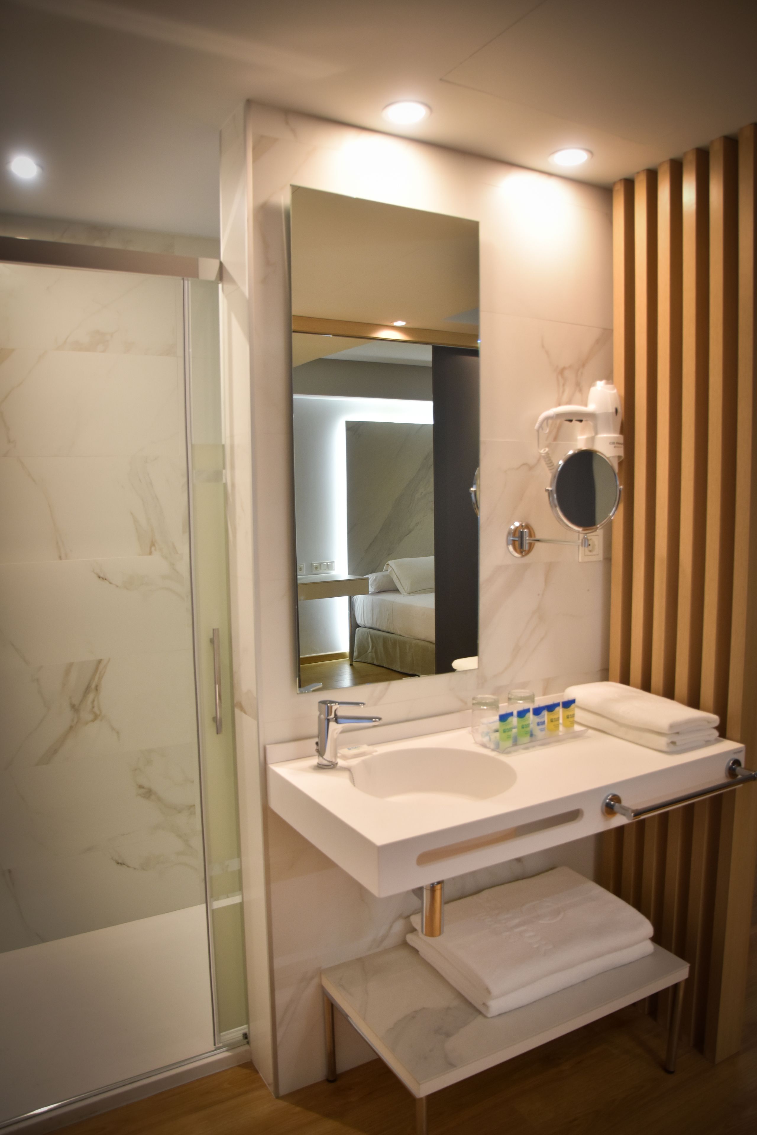 Un baño moderno con cabina de ducha de vidrio, lavabo blanco con tocador, espejo y toallero.