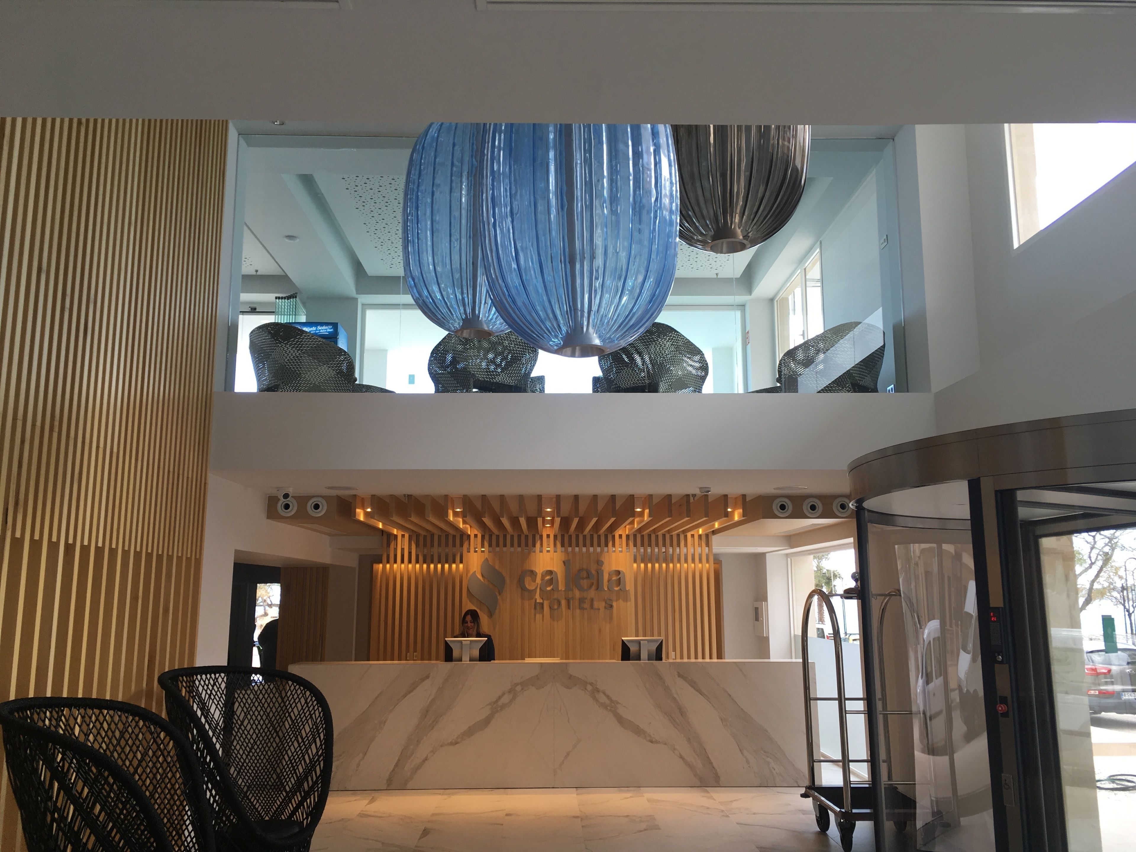 A hotel reception area with a marble counter, a receptionist, and a modern chandelier.