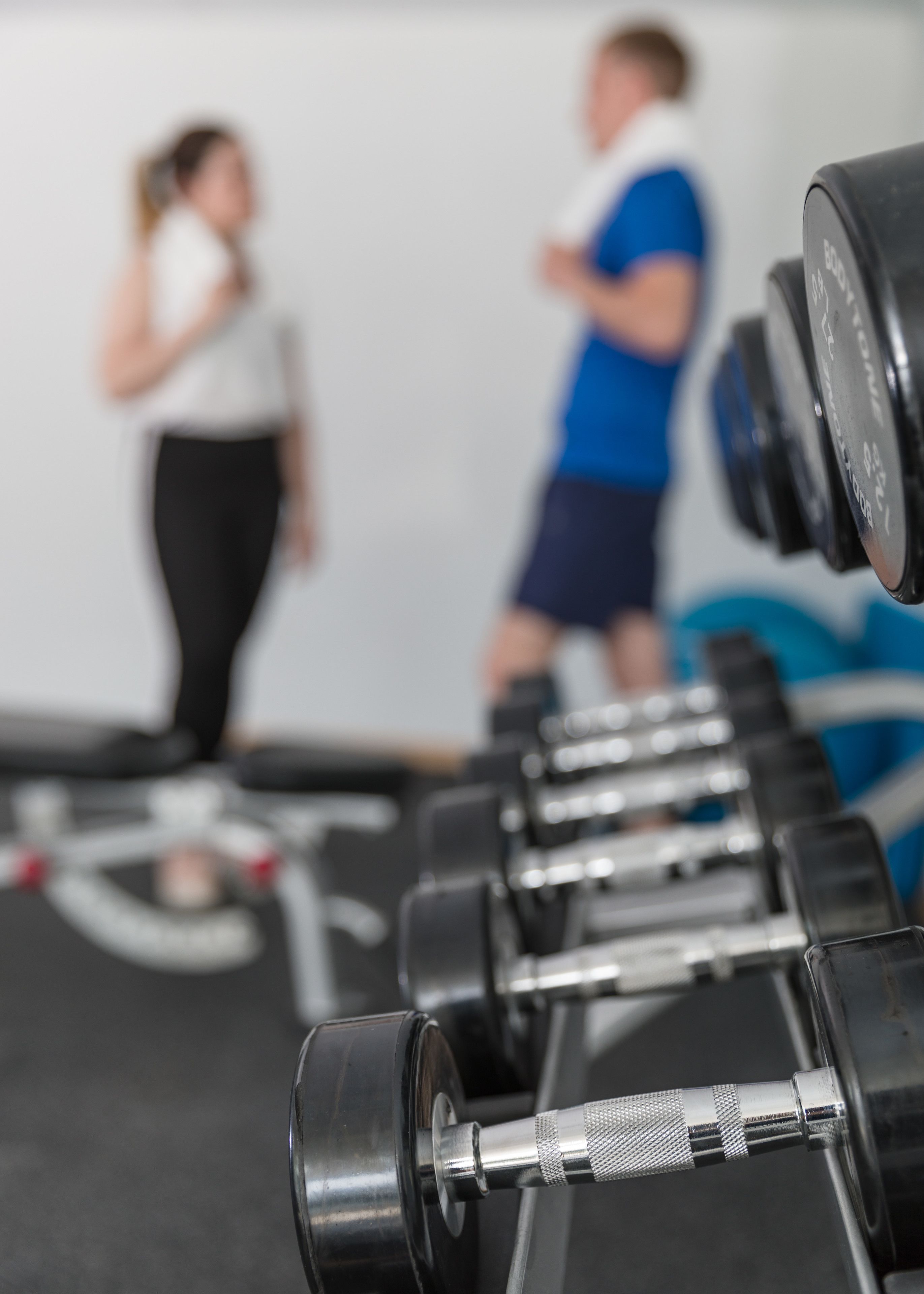 Un gimnasio con equipo de ejercicio y dos personas al fondo.