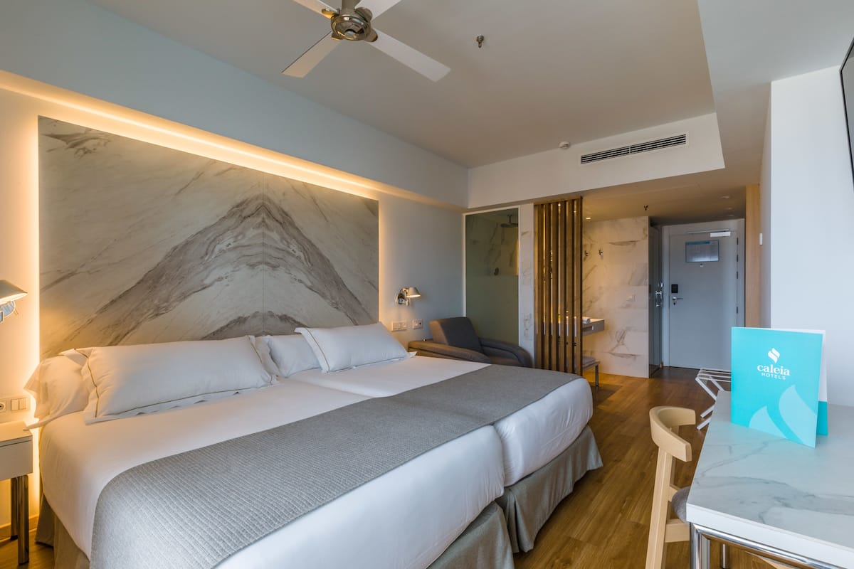 A modern hotel room with a large bed, a desk, and a marble wall.