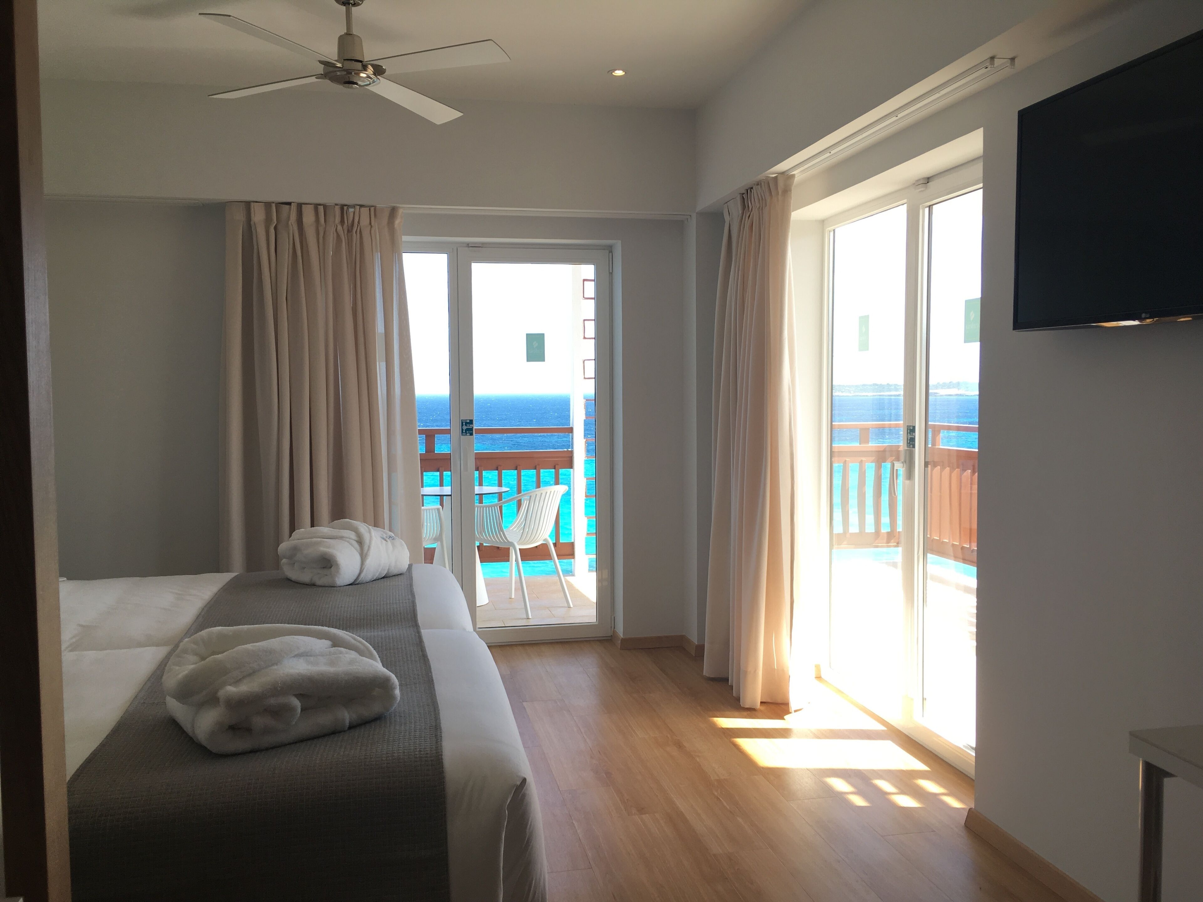 Ein Hotelzimmer mit Bett, Deckenventilator, Fernseher und einem Balkon mit Meerblick.