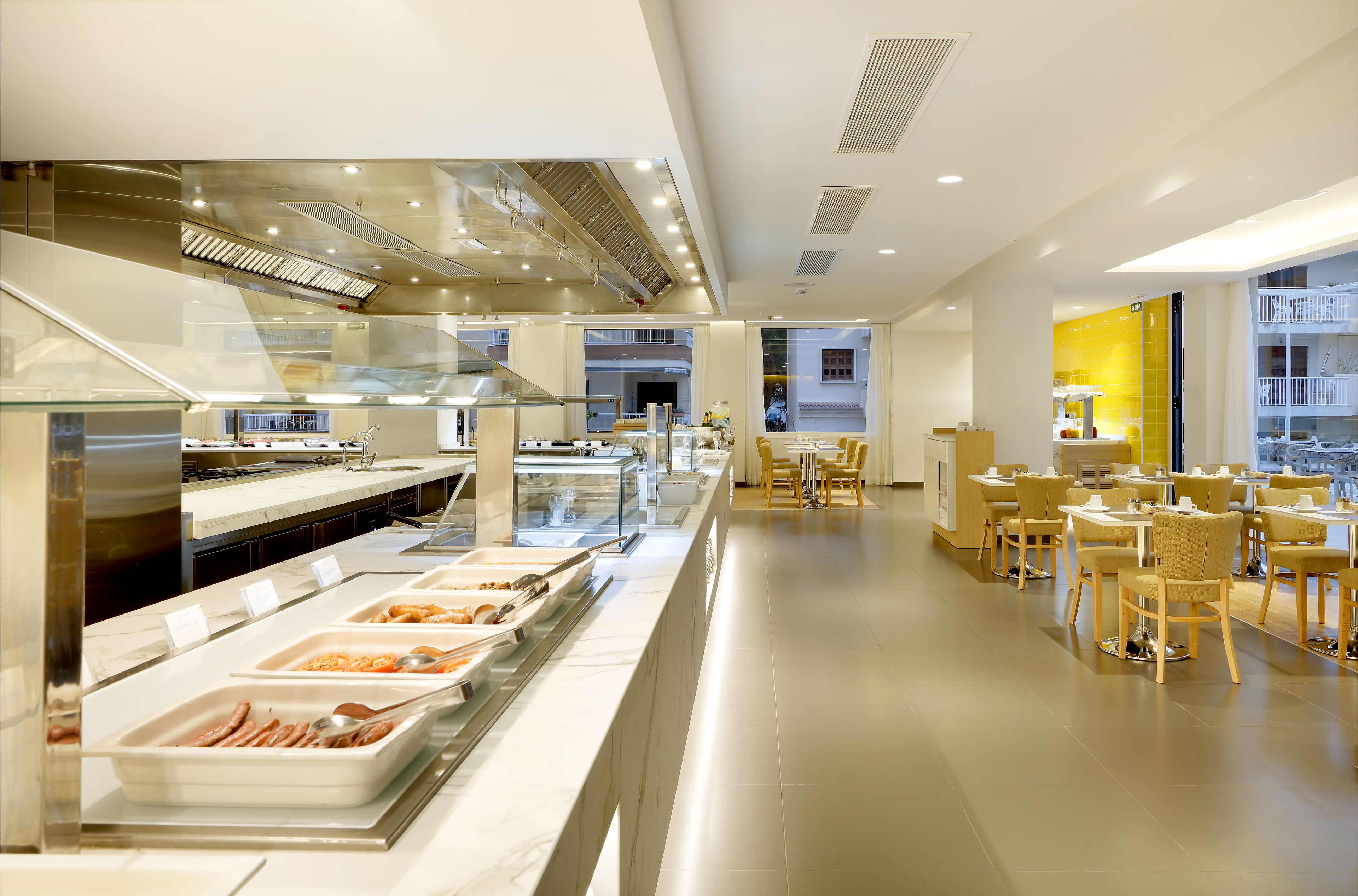 Un comedor moderno de hotel con bufé, disposición de mesas y vistas a la ciudad.