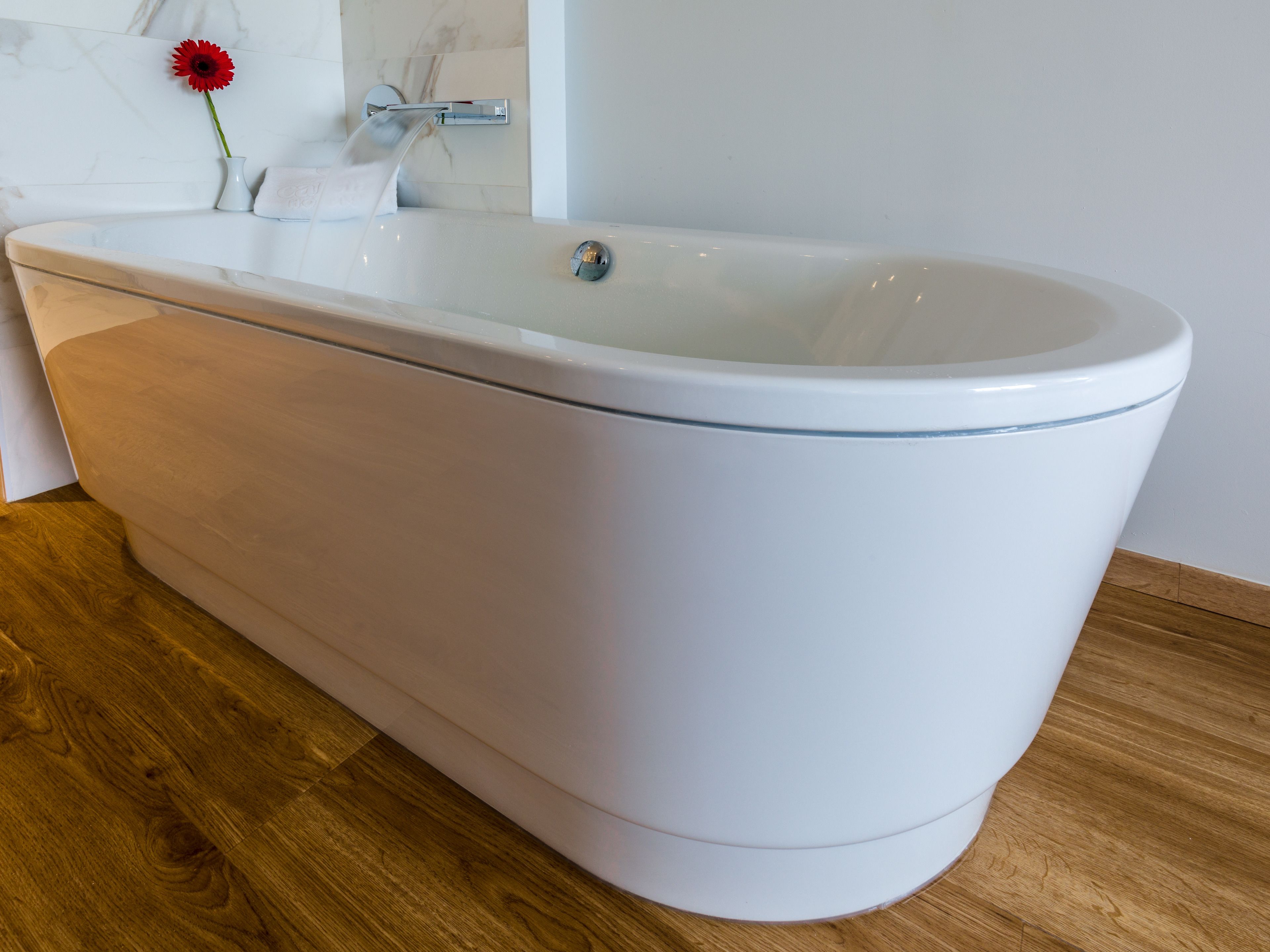 A modern bathroom with a freestanding bathtub, a wooden floor, and a marble wall.