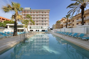 Relax by the pool surrounded by palm trees and a low wall.
