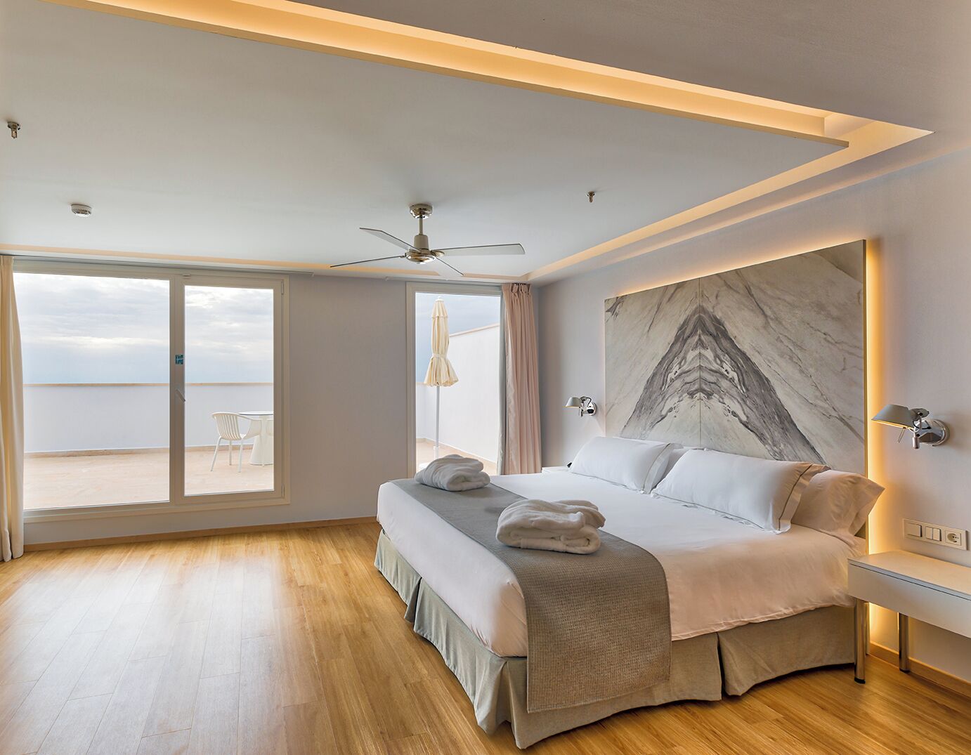 Un dormitorio moderno con una cama grande, un ventilador de techo y vista al mar a través de un ventanal corredero.