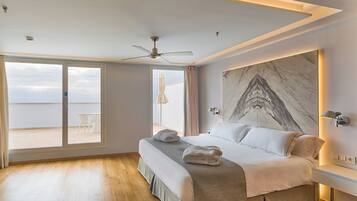 Un dormitorio moderno con una cama grande, un ventilador de techo y vista al mar a través de un ventanal corredero.