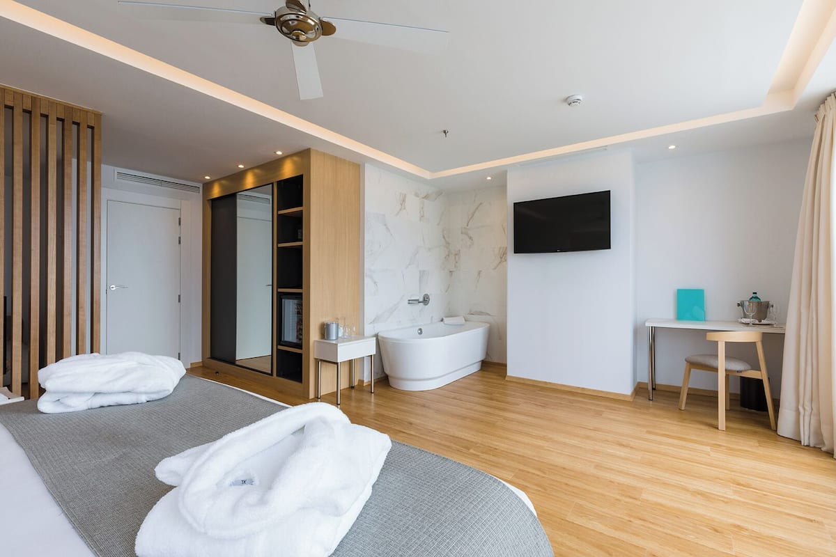 Une chambre d’hôtel moderne équipée d’un lit, d’une salle de bain avec baignoire, d’un bureau et d’un téléviseur à écran plat.