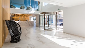 Un moderno vestíbulo de hotel con piso de mármol, una recepción, una silla negra y una puerta giratoria.