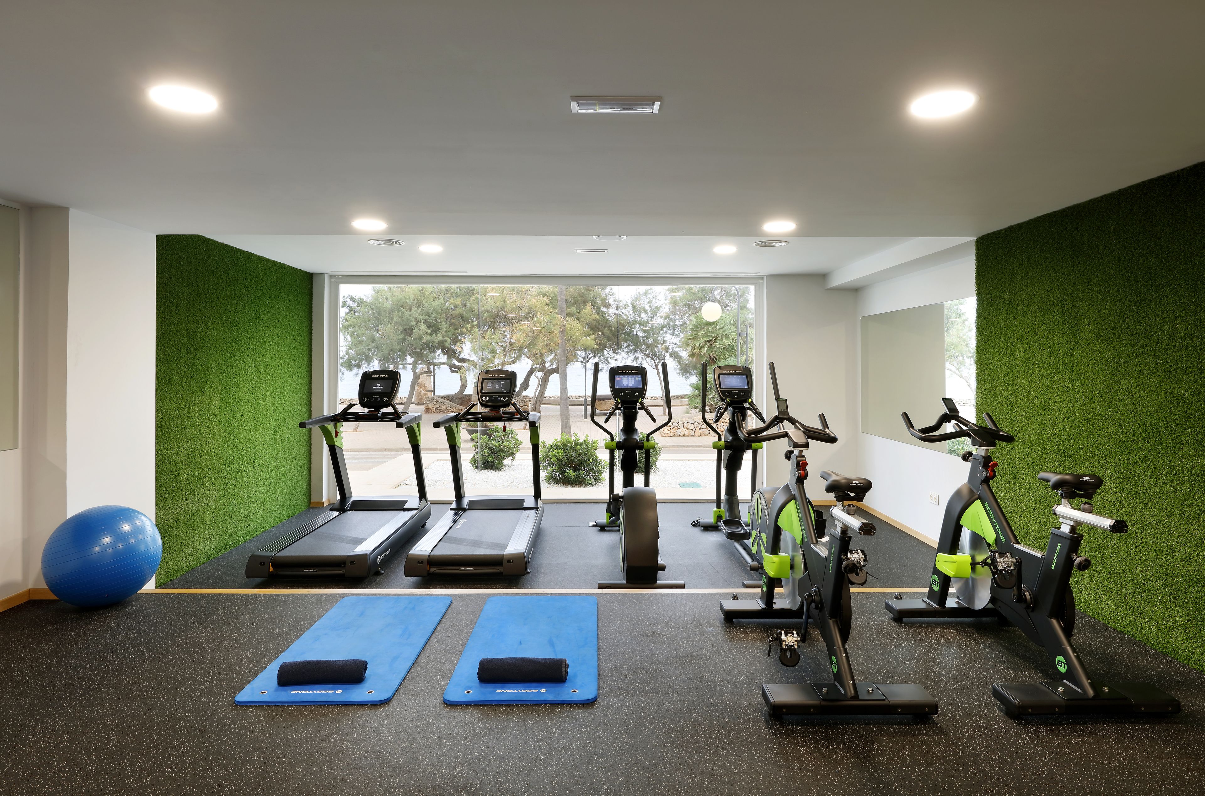 Un gimnasio con cintas de correr, bicicletas estáticas y colchonetas de ejercicio.