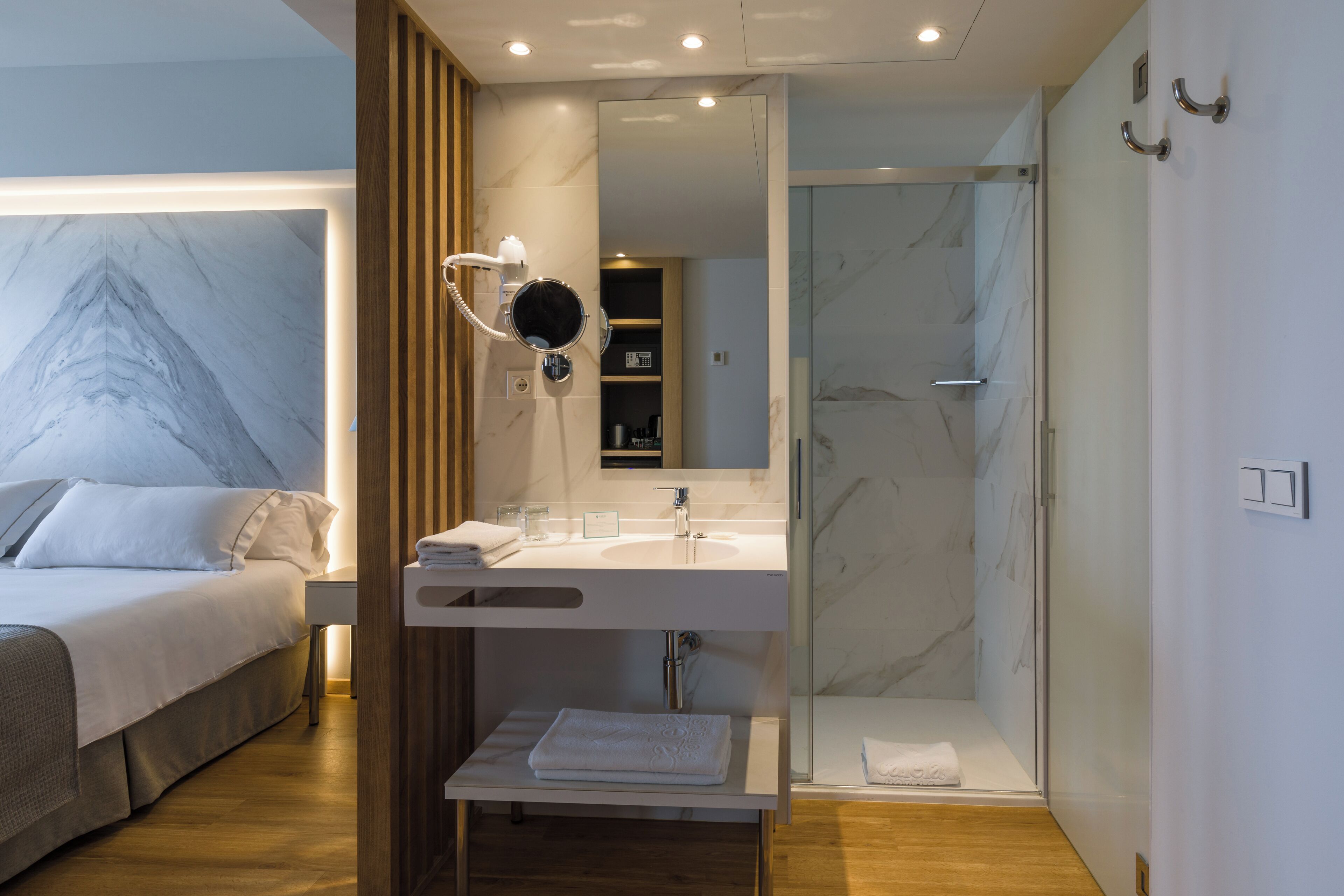 Una habitación de hotel moderna con una cama, un baño con ducha de vidrio y un tocador con espejo.