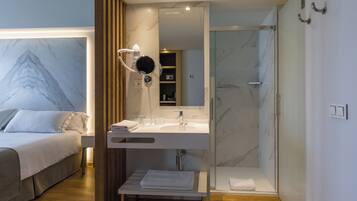 Una habitación de hotel moderna con una cama, un baño con ducha de vidrio y un tocador con espejo.