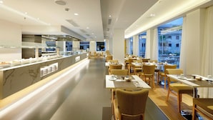 Un restaurante moderno con una barra alargada, varias mesas para comer y sillas.
