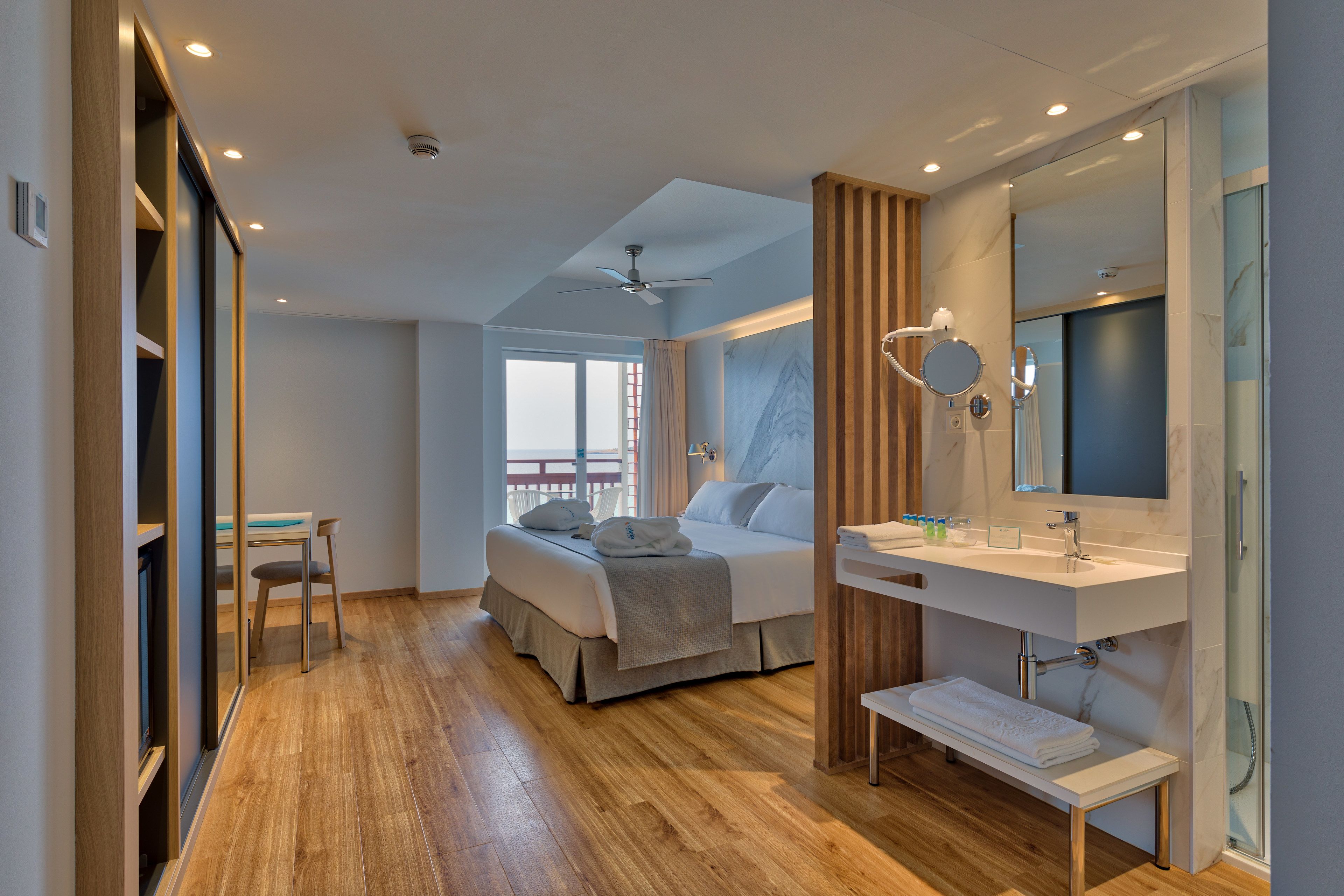A modern bedroom with a bed, bedside table, and a bathroom with a sink and mirror.