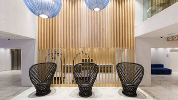 Eine moderne Lobby mit drei schwarzen Korbstühlen, einer Wand aus Holzleisten und einem blauen Sofa im Hintergrund.
