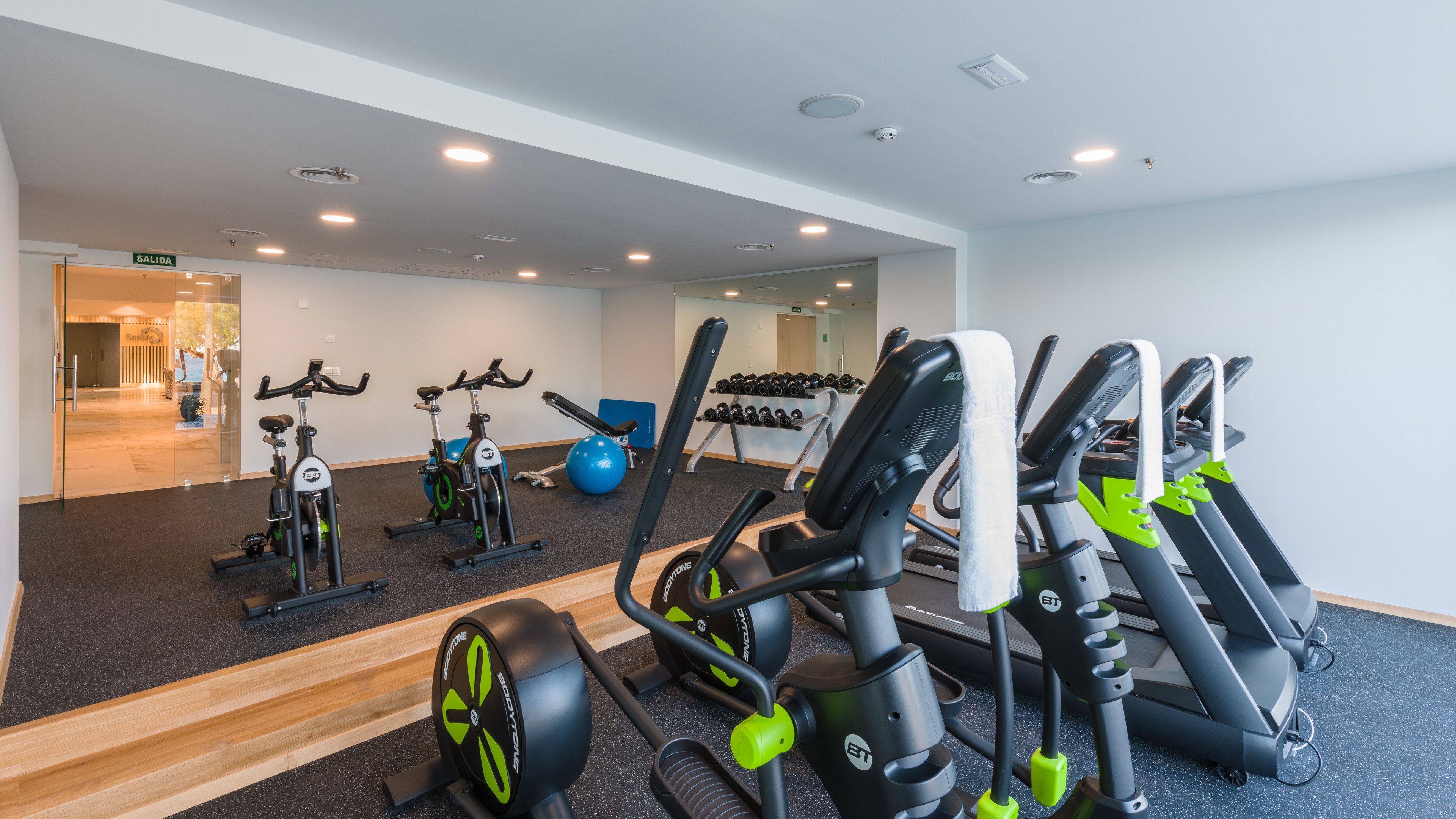 Un gimnasio con varios equipos de ejercicio, incluyendo cintas de correr, bicicletas estáticas y máquinas de pesas.