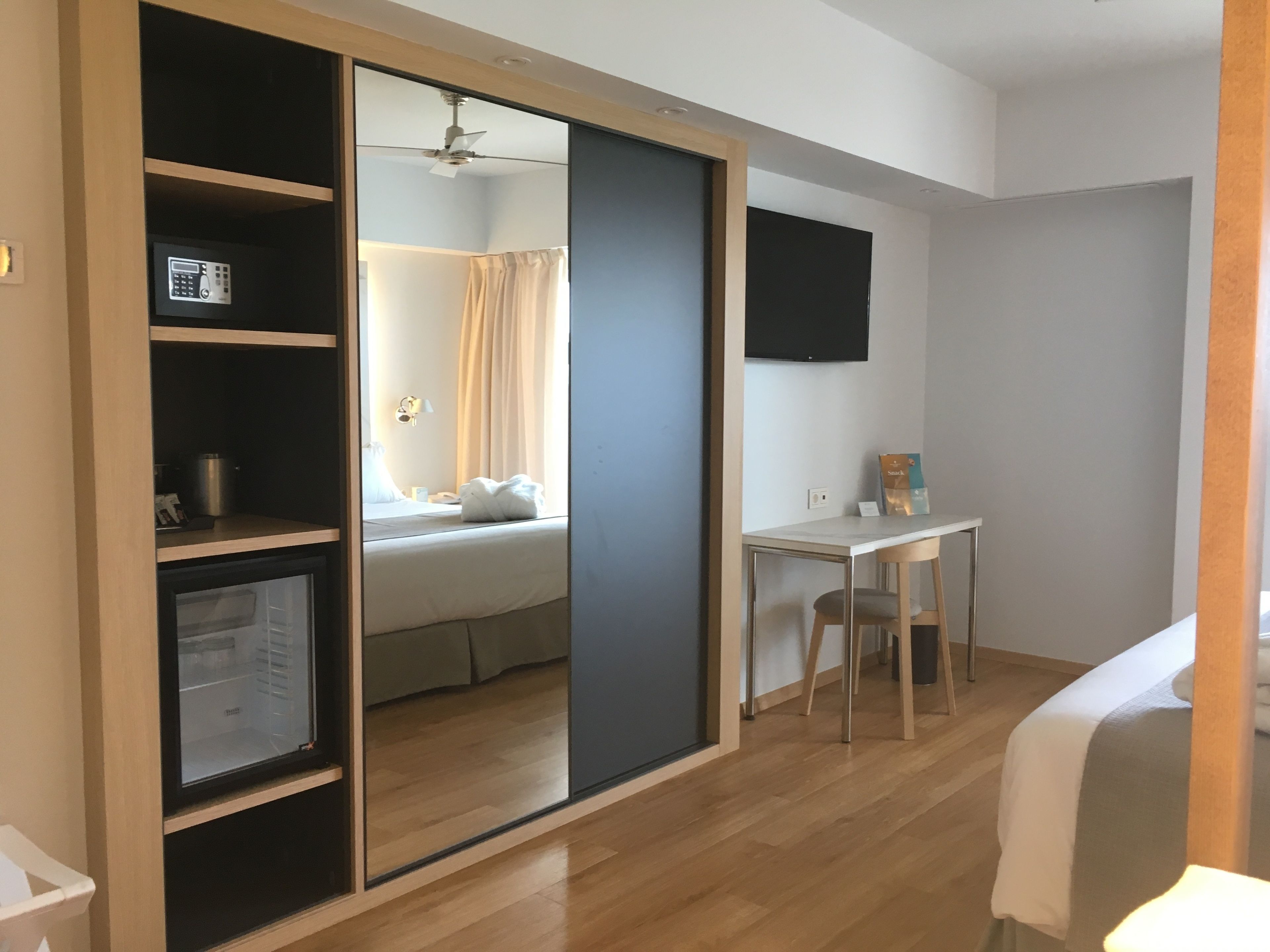 Una habitación de hotel con armario corredera, cama, escritorio y televisor fijado a la pared.