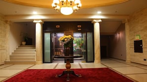 Eine Lobby mit rotem Teppich, einer Kristallleuchter, einer Treppe und einem Empfangsbereich mit Blumen.