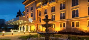 A hotel with a fountain, a covered entrance, and a sign reading 'SHIMANO GARDEN.'