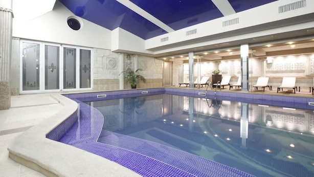 Ein Innenpool mit blau gefliestem Rand, einer Decke mit blauen Paneelen und Liegestühlen am Pool.