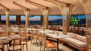 A restaurant with multiple dining areas, including booths and tables, with a view of the cityscape. - Zeus Kos Beach (Kos)