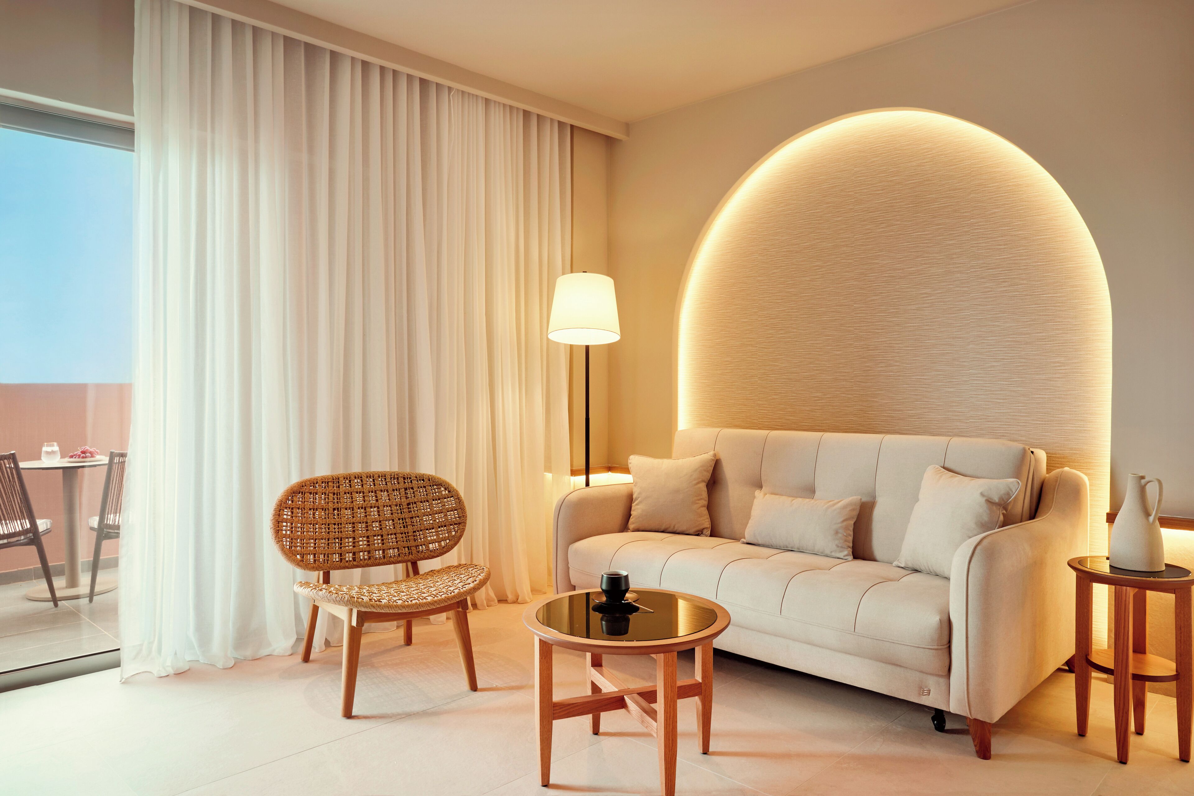 A modern living room with a sofa, a round coffee table, a wicker chair, and a lamp.