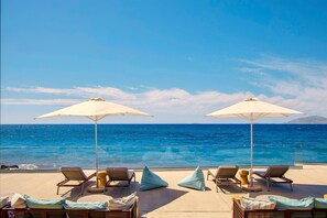 A sunlit outdoor seating area with lounge chairs and umbrellas overlooking the ocean.