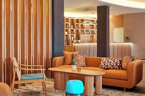 Un espace de détente moderne avec un canapé en bois, une chaise en bois et une petite table. On aperçoit en arrière-plan une bibliothèque remplie de divers objets.