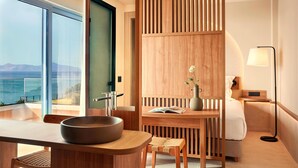 A modern hotel room with a large window, a wooden desk, a bowl sink, a bedside table with a lamp, and a view of the sea. - Zeus Kos Beach (Kos)