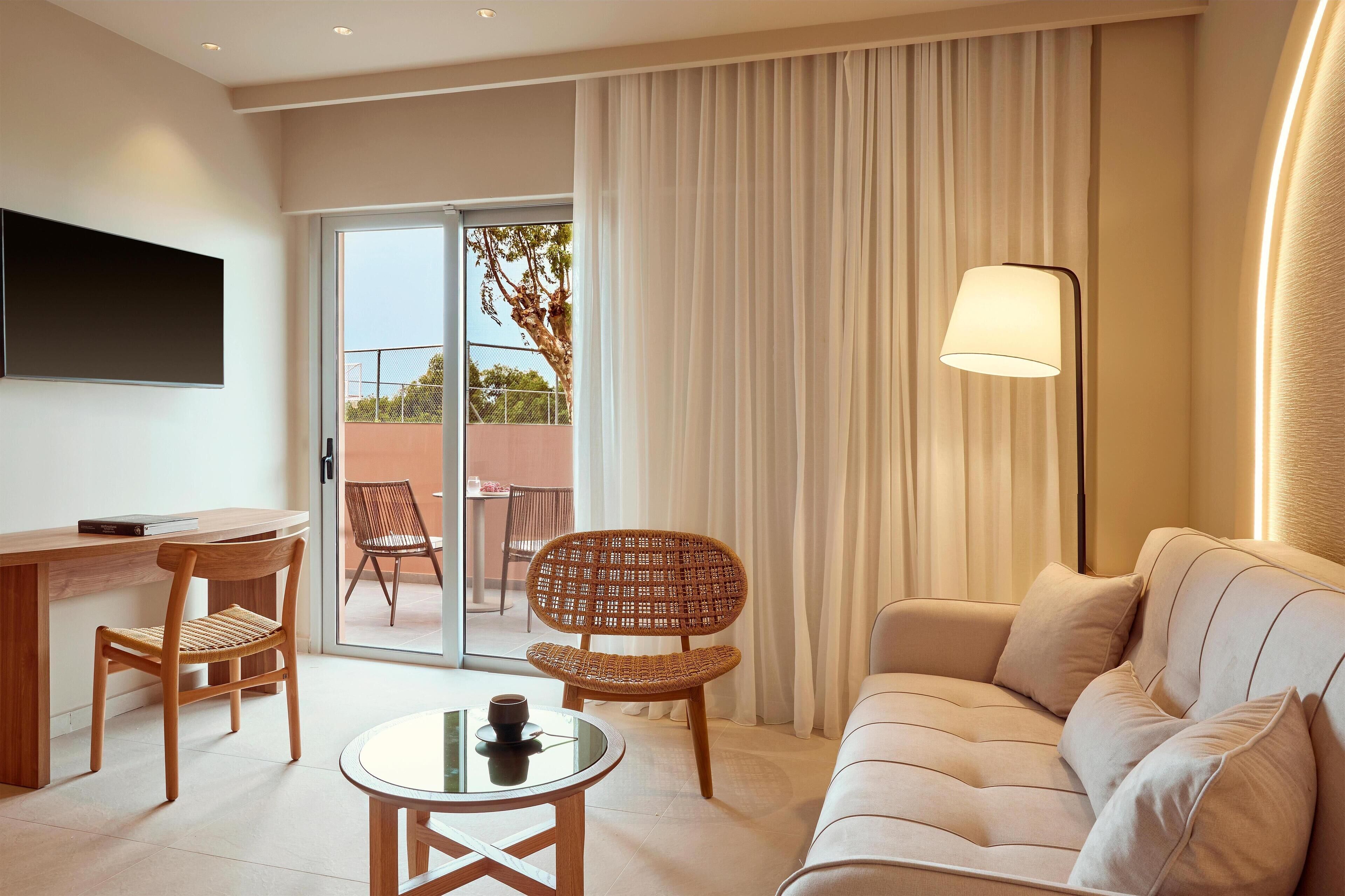Une chambre d’hôtel moderne équipée d’un canapé, d’une table à manger avec des chaises, d’un téléviseur à écran plat fixé au mur et d’une grande fenêtre avec des rideaux.