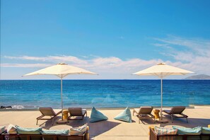 A sunlit outdoor seating area with lounge chairs and umbrellas overlooking the ocean. - Zeus Kos Beach (Kos)