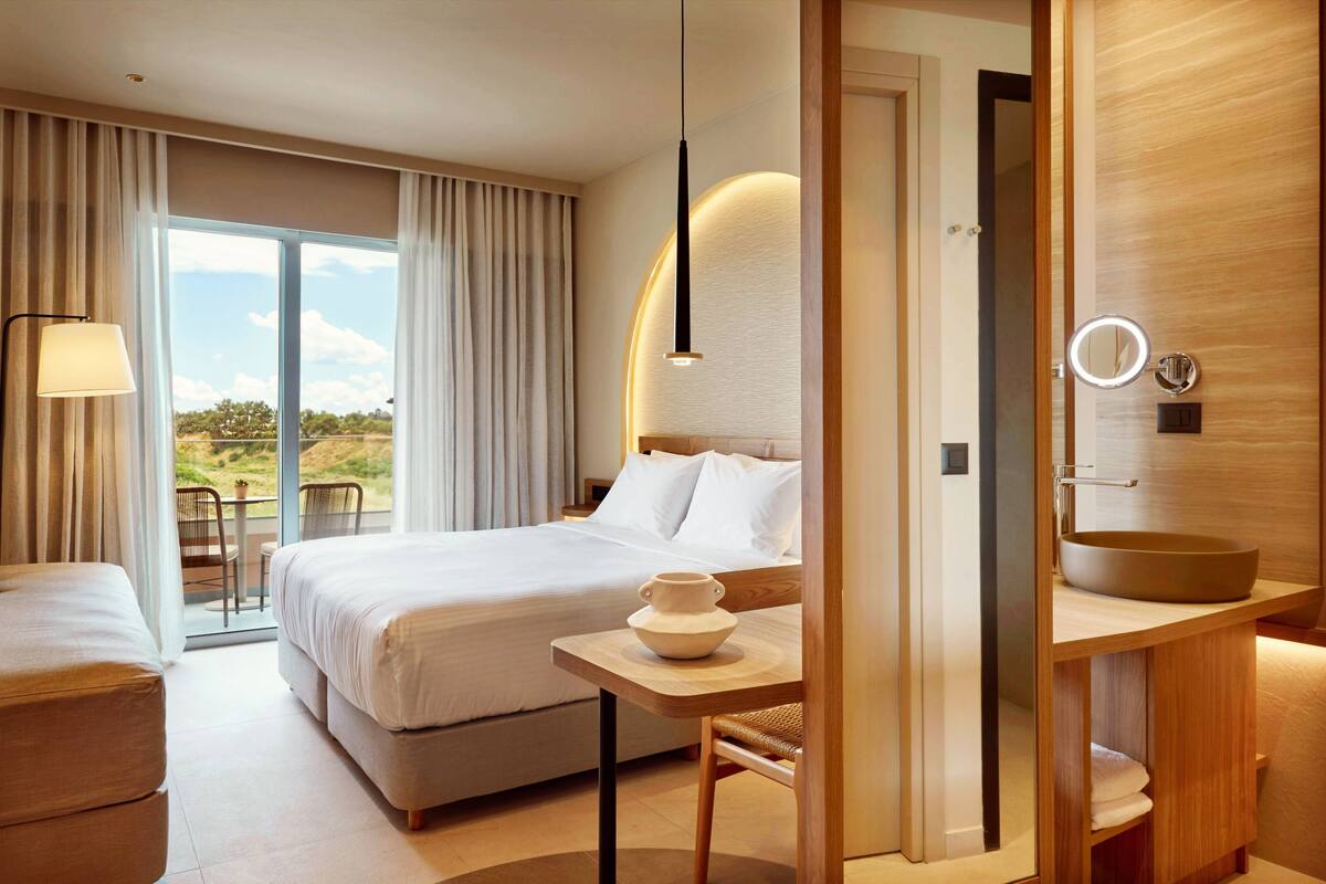 Habitación de hotel con cama, una mesa con una taza, un espejo y vistas al exterior.