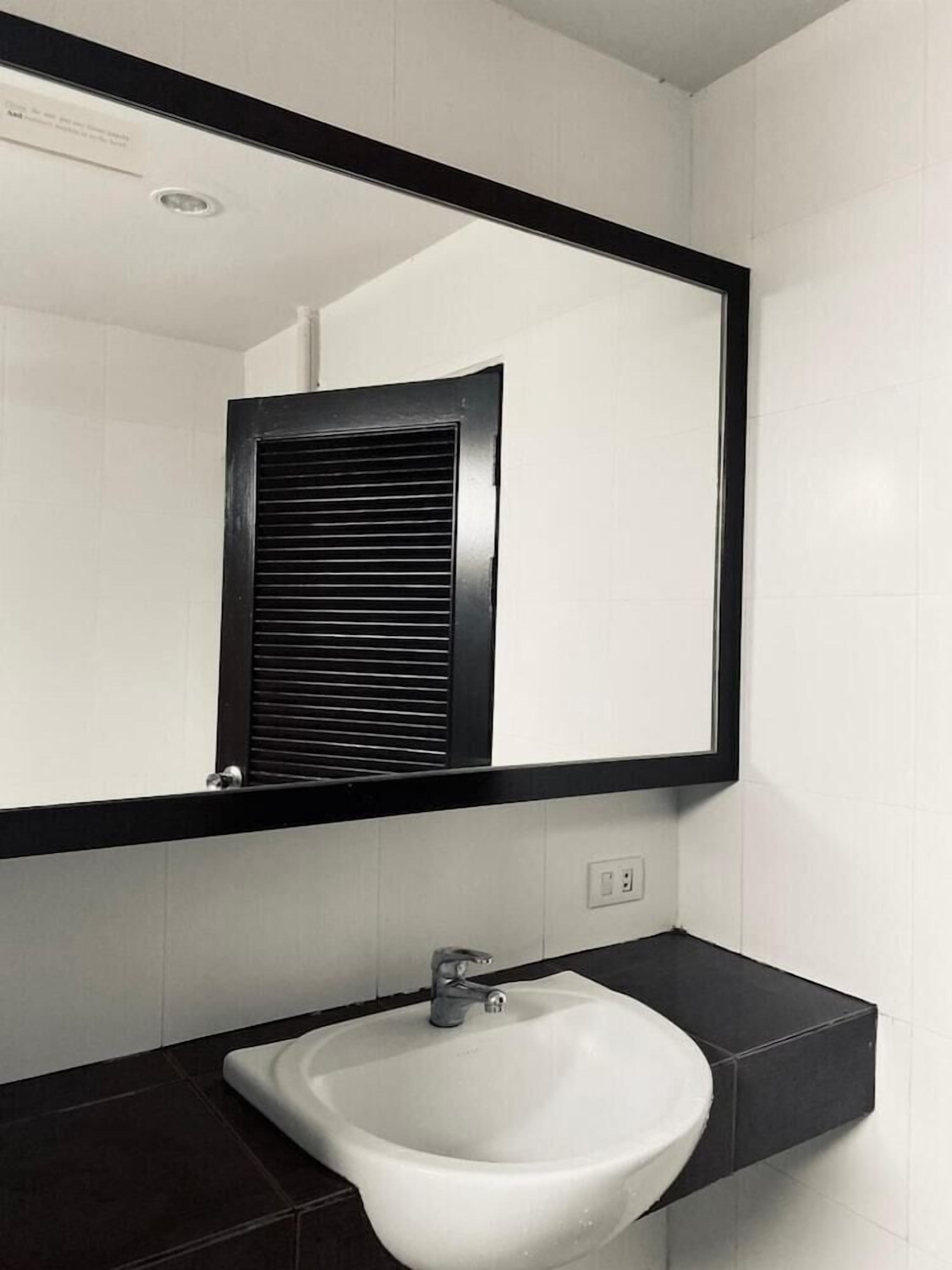 A bathroom with a white sink, a black-framed mirror, and a ventilation unit.