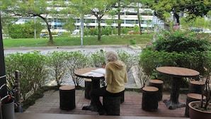 A person sitting at a round table with a view of a street and greenery. - Putra One Avenue Hotel (Seri Kembangan)