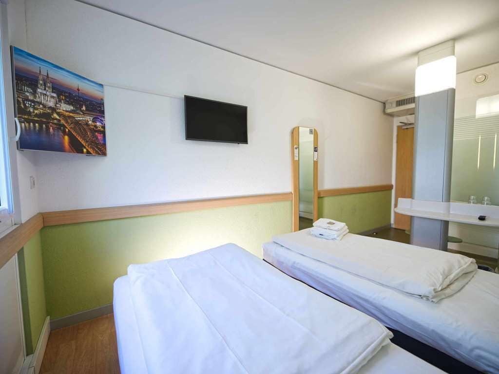 A hotel room with two beds, a television, a mirror, and a painting of a cityscape.