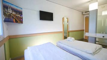 Une chambre d’hôtel avec deux lits, une télévision, un miroir et un tableau représentant un paysage urbain.