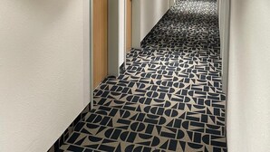 En hotels korridor med mønstret gulv, døre og en brandslukker.