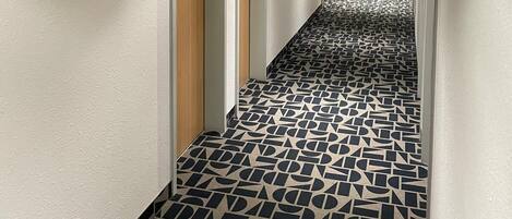 Un pasillo de hotel con suelo estampado, puertas y un extintor.