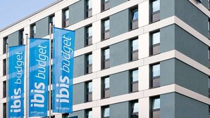 En moderne bygning med mange vinduer og tre blå bannere, der reklamerer for "Ibis Budget" og "WLAN gratis".