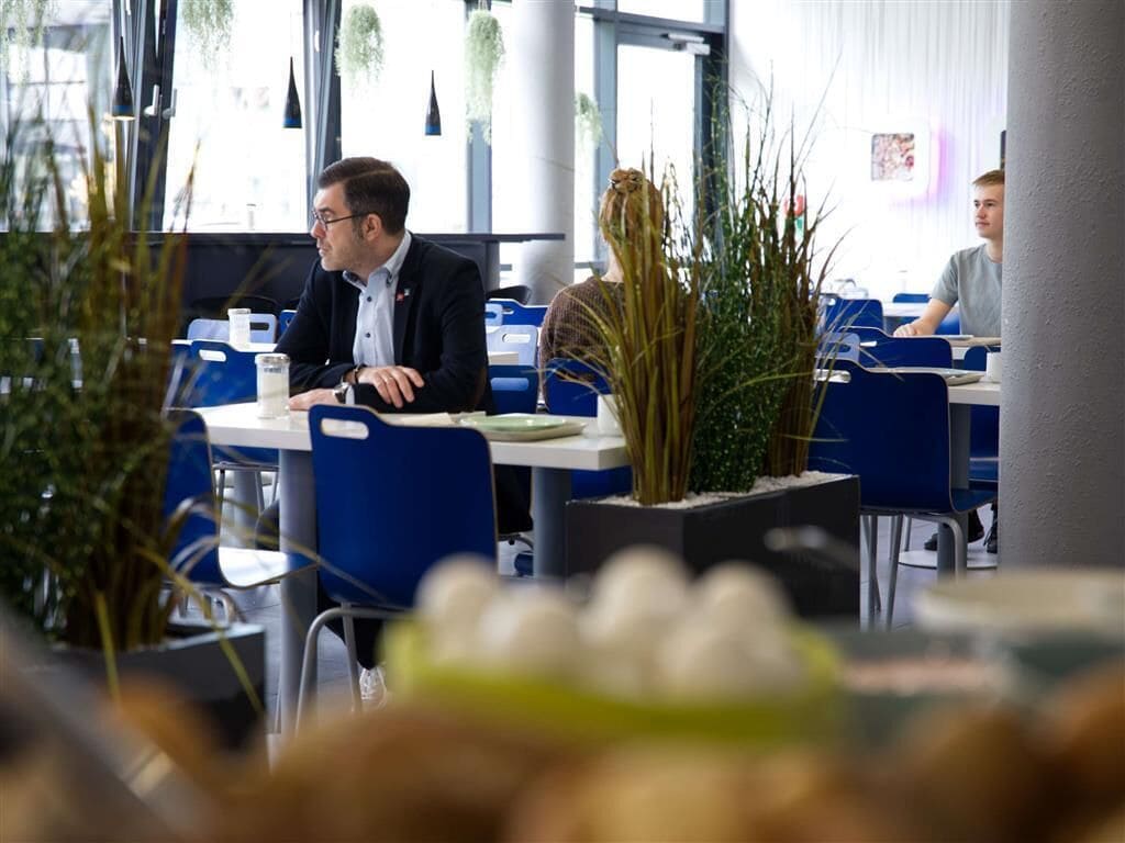 A modern dining area with blue chairs and tables, a potted plant, and a person seated at a table.