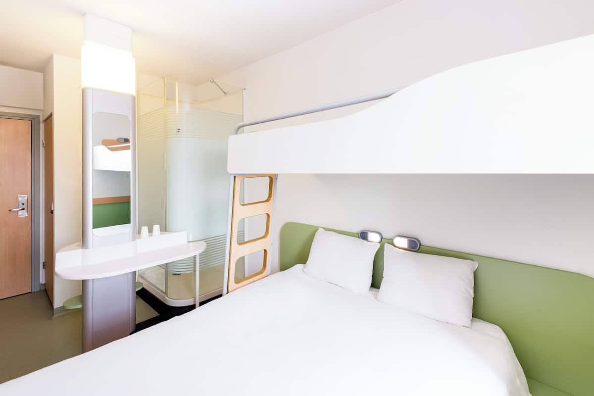 A modern hotel room with a bunk bed, a small desk with a chair, and a bedside table.