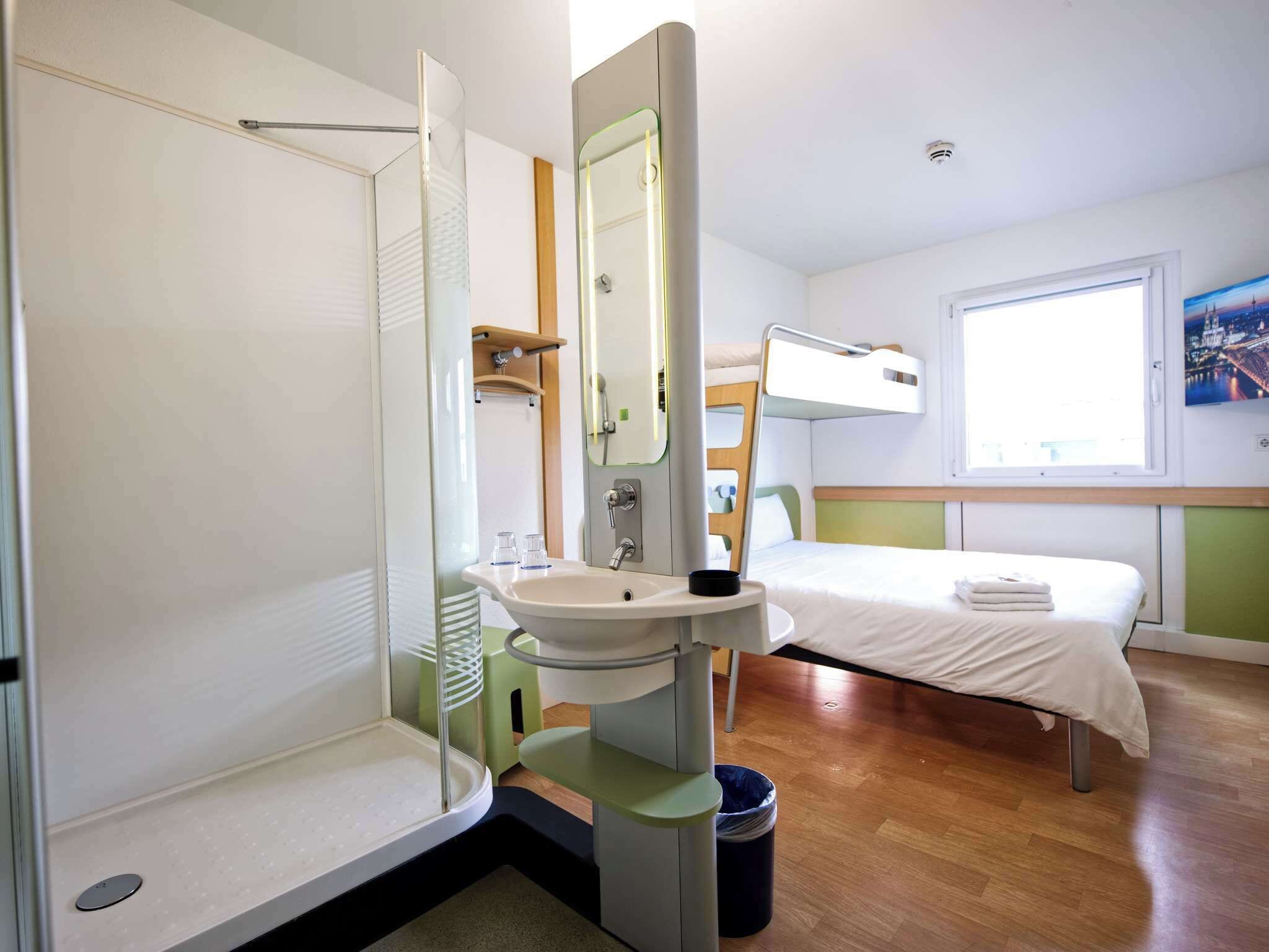 Et lille hotelværelse med bruser, håndvask og køjeseng.