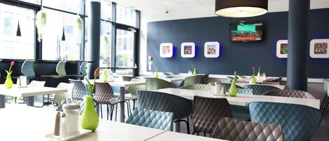 Un restaurante moderno con mesas altas, sillas acolchadas, ventanas amplias y un televisor montado en la pared.