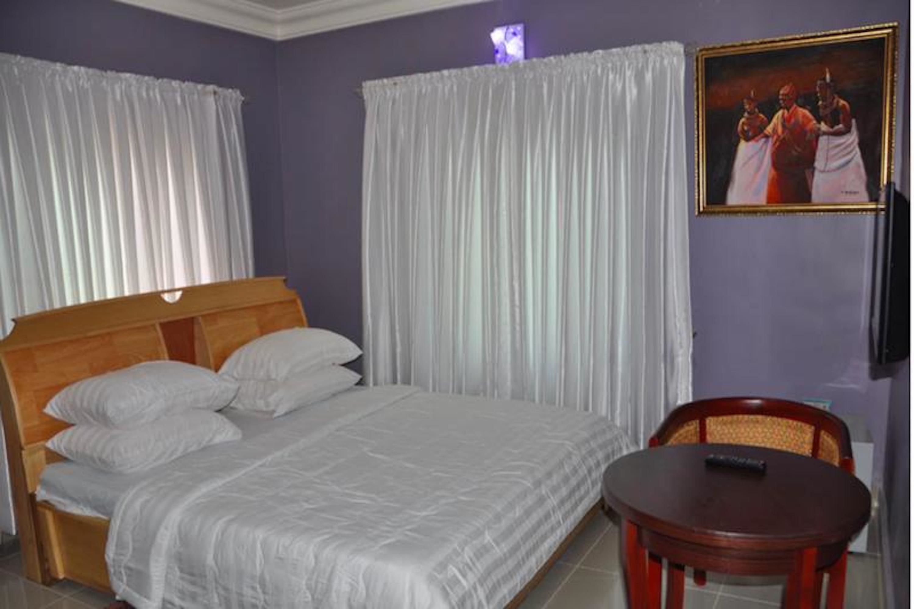 A bedroom with a bed, curtains, a painting, and a table.