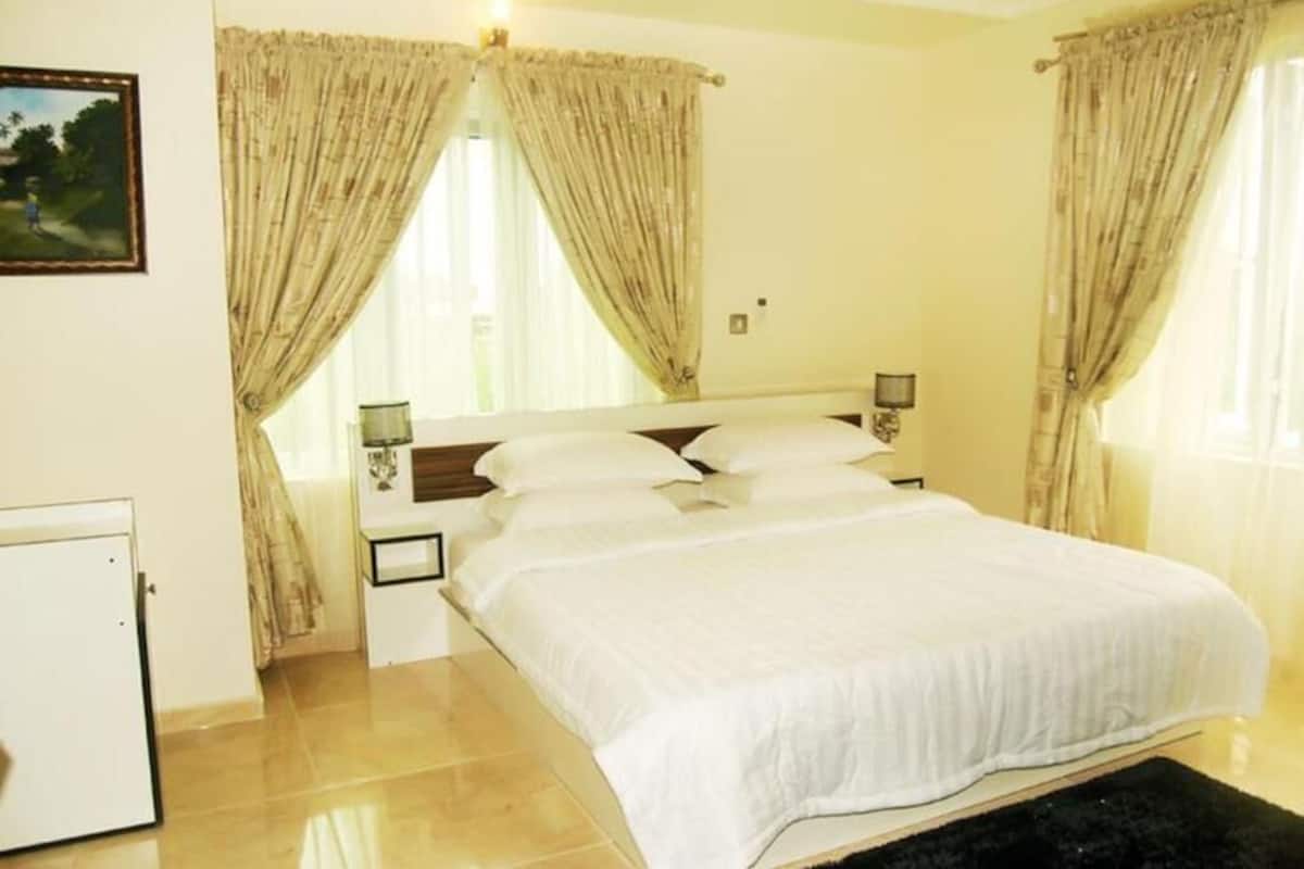 A bedroom with a bed, curtains, a nightstand, a lamp, and a wall-mounted TV.