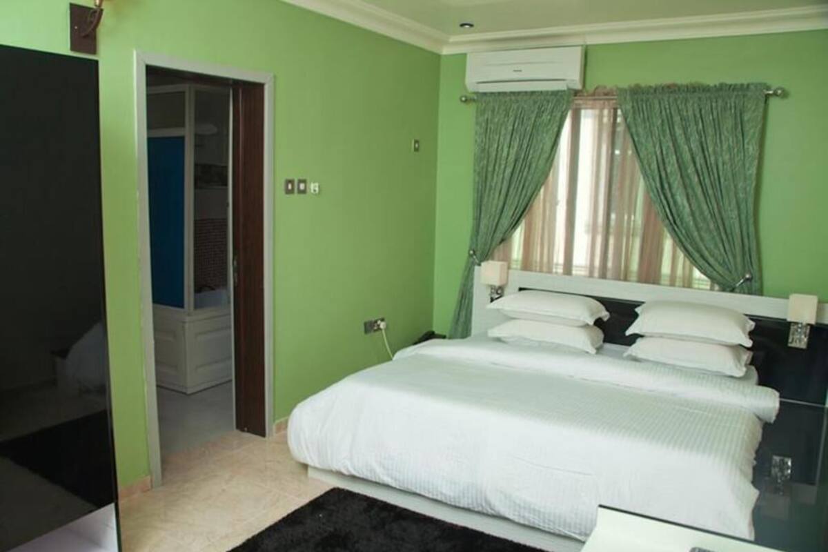 A bedroom with a bed, a bedside table, a mirror, and a window with curtains.