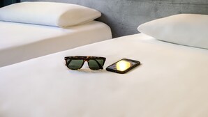 A hotel room with two beds, a headboard with built-in lighting, and a pair of sunglasses and a smartphone on the bed. - ibis budget Bordeaux Centre Gare Saint Jean (Bordeaux)